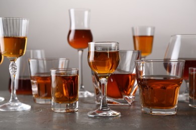 Photo of Different delicious liqueurs in glasses on grey table