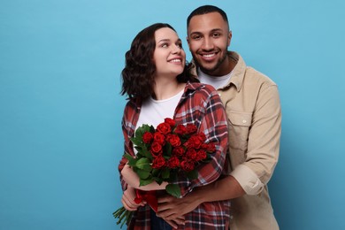 Photo of Happy couple celebrating Valentine's day. Beloved woman with bouquet of red roses on light blue background. Space for text