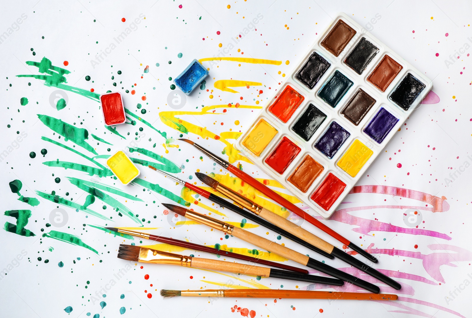 Photo of Plastic palette with colorful paints and brushes on light background, top view