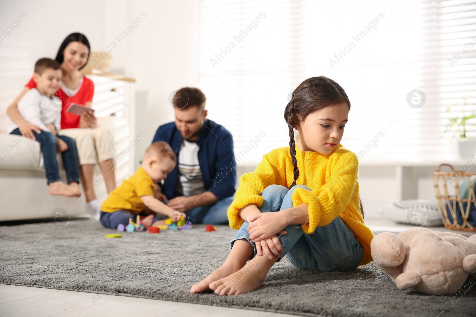 Photo of Unhappy little girl feeling jealous while parents spending time with other children at home