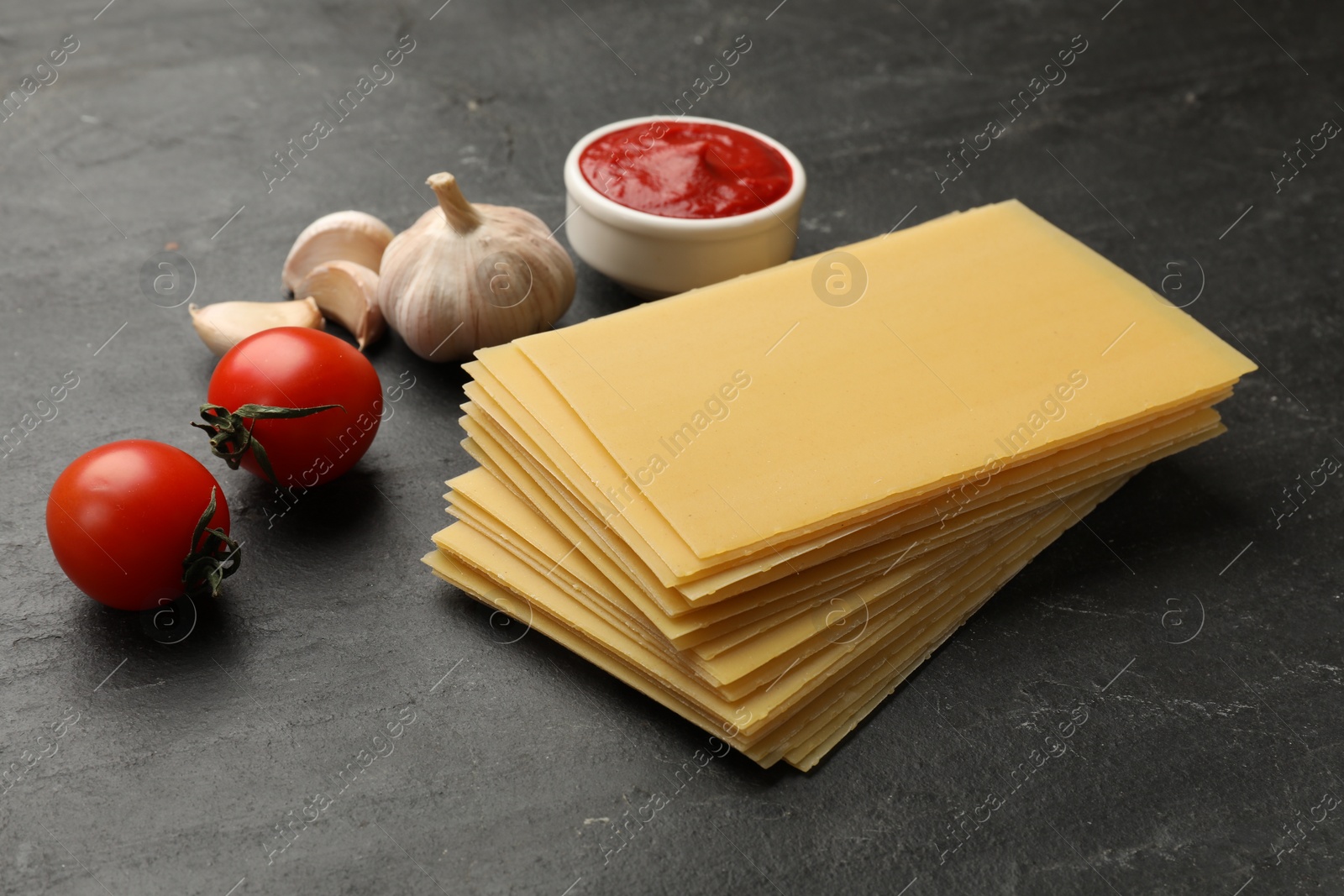 Photo of Cooking lasagna. Pasta sheets, tomato, garlic and ketchup on dark textured table