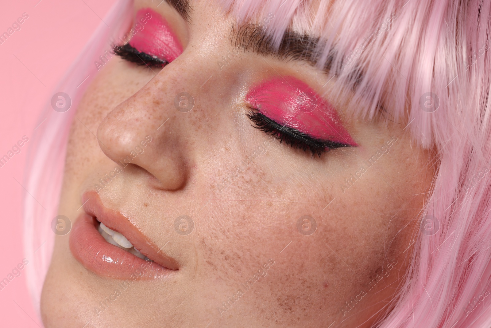 Photo of Beautiful woman with bright makeup and fake freckles on pink background, closeup