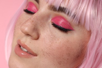 Beautiful woman with bright makeup and fake freckles on pink background, closeup