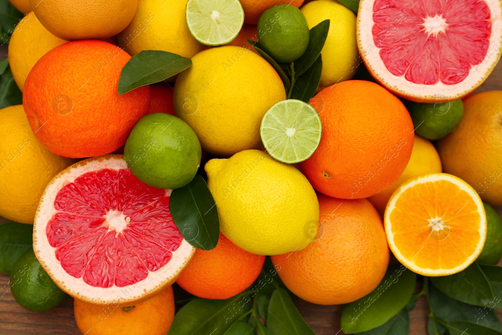 Photo of Different citrus fruits with green leaves on wooden table, top view