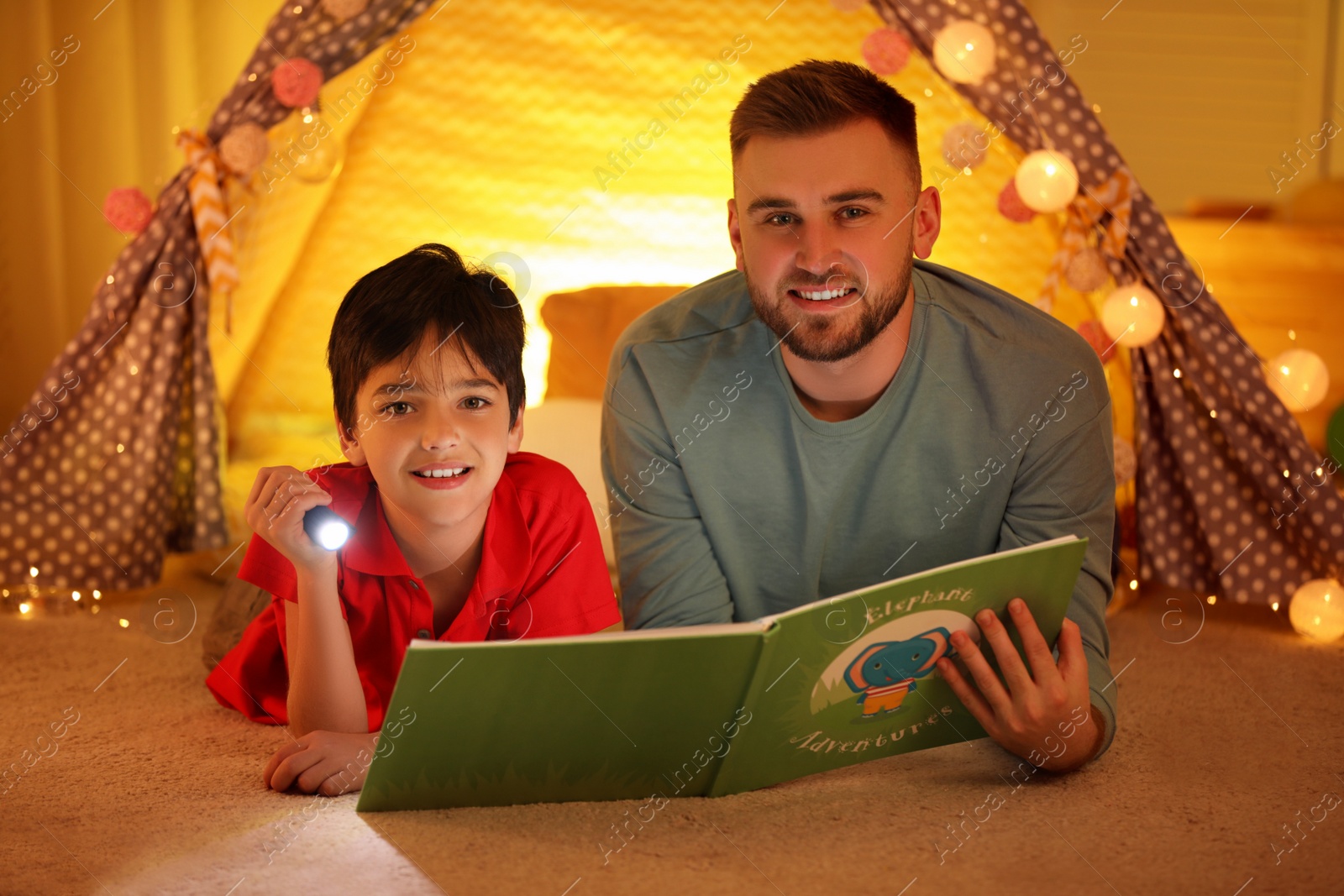 Photo of Father and son with flashlight reading book at home