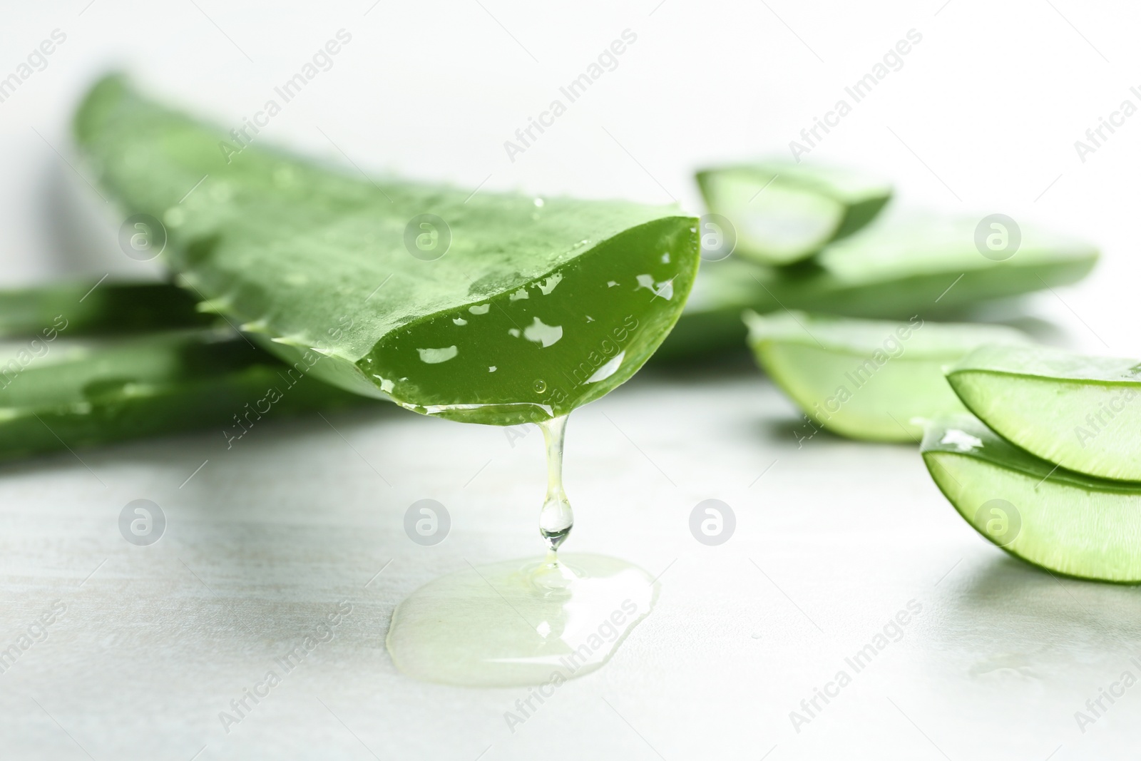 Photo of Fresh sliced aloe vera leaf with dripping juice on light table, closeup