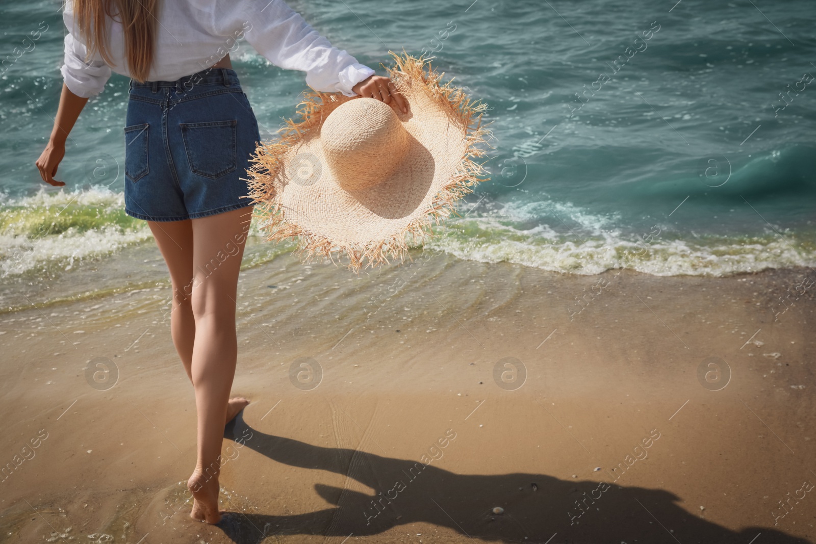 Photo of Young woman with straw hat near sea on sunny day in summer, closeup back view