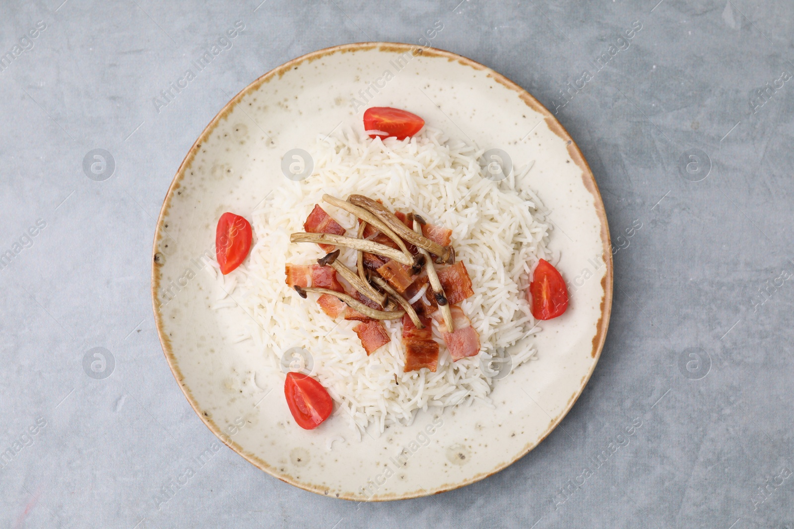 Photo of Delicious rice with bacon, mushrooms and tomatoes on gray table, top view