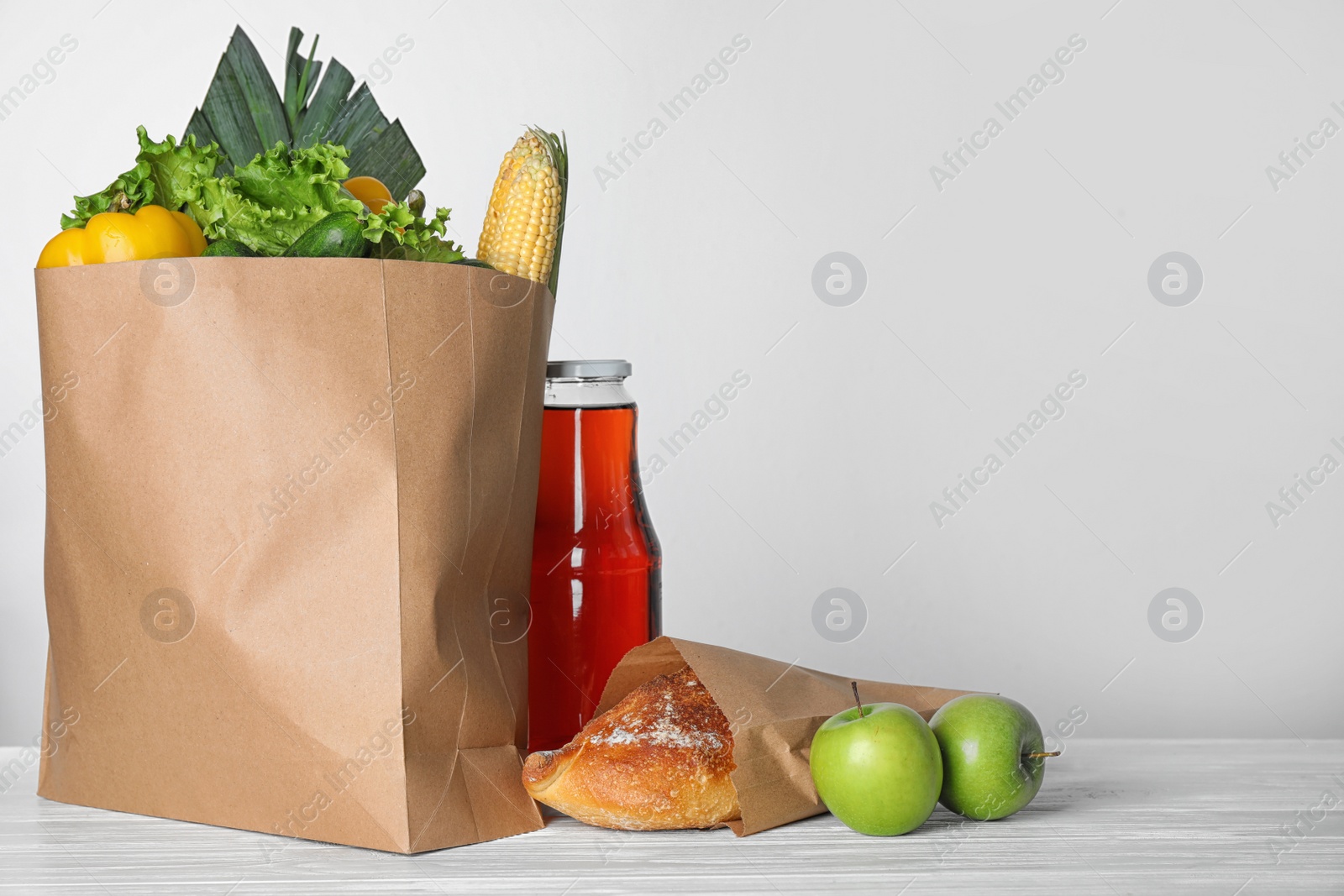 Photo of Paper bag with fresh vegetables and other products on white wooden table against light background, space for text