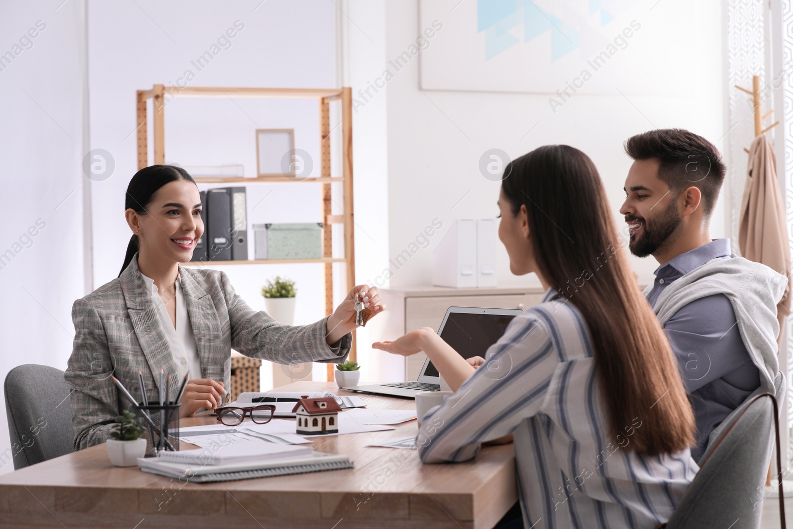 Photo of Real estate agent giving house key to young couple in office. Mortgage concept