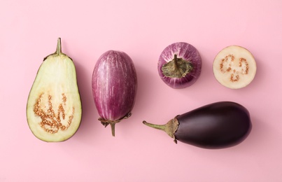 Cut and whole raw ripe eggplants on pink background, flat lay