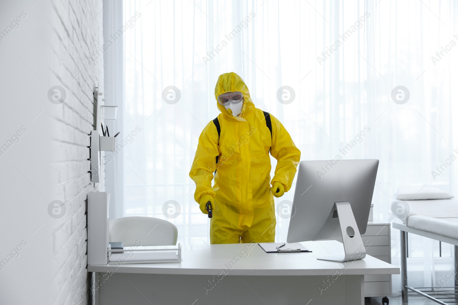 Photo of Employee in protective suit sanitizing doctor's office. Medical disinfection