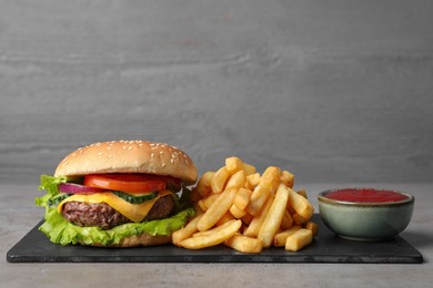 Delicious burger, ketchup and french fries served on grey table