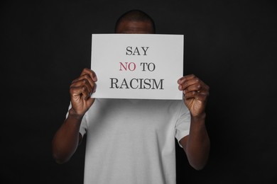 African American man holding sign with phrase Say No To Racism on black background