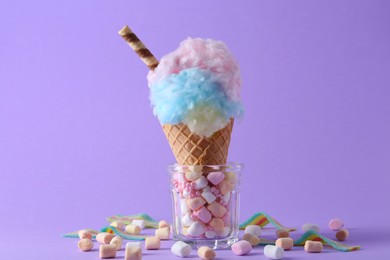 Photo of Sweet cotton candy in waffle cone and marshmallows on purple background, closeup