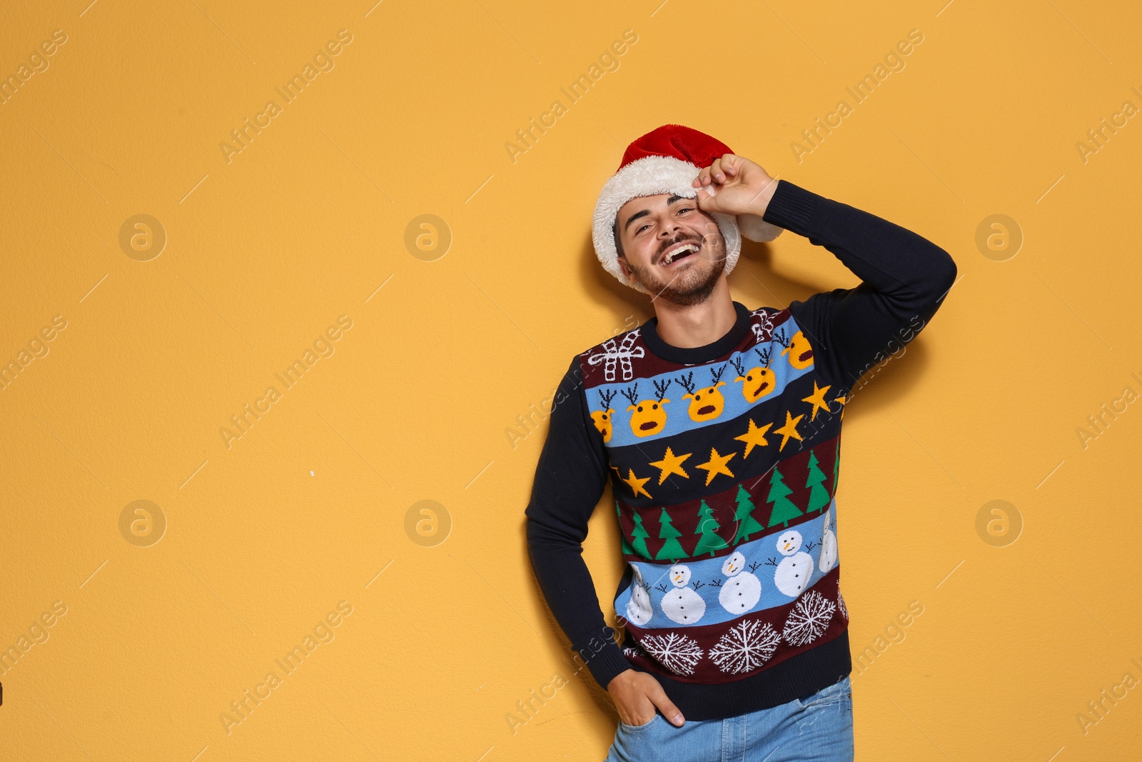 Photo of Young man in Christmas sweater and hat on color background. Space for text