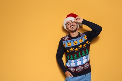 Young man in Christmas sweater and hat on color background. Space for text