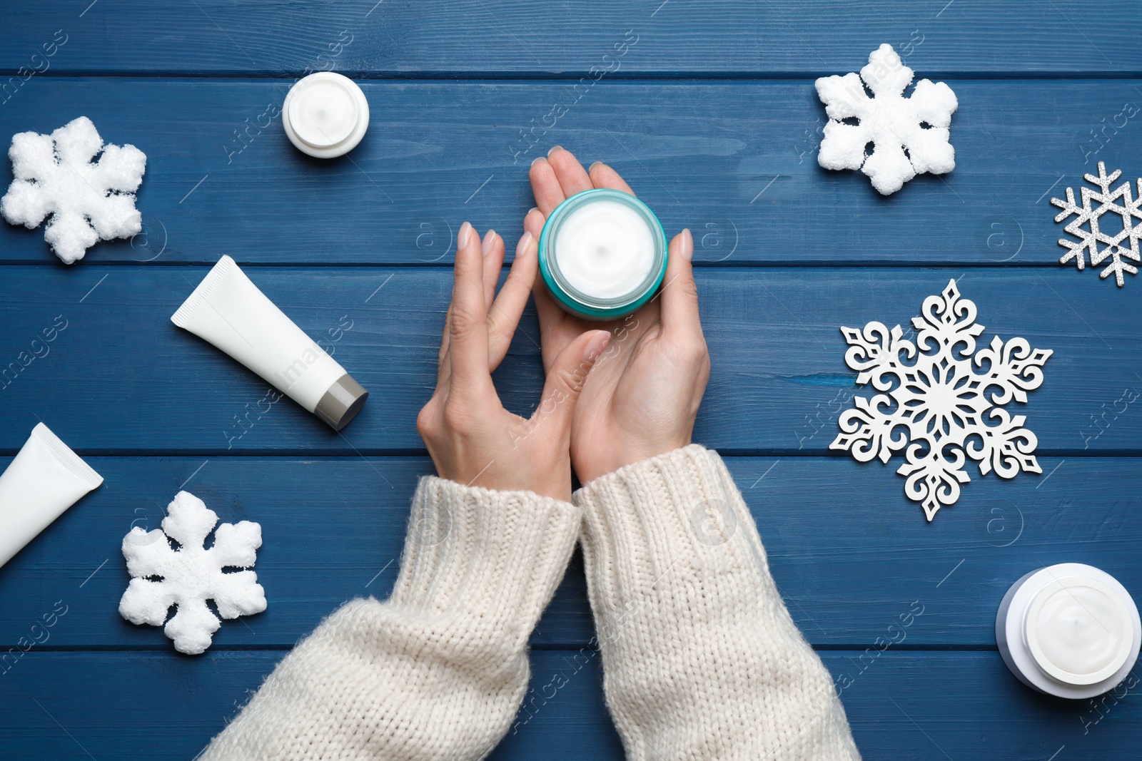 Photo of Woman with jar of hand cream at blue wooden table, top view