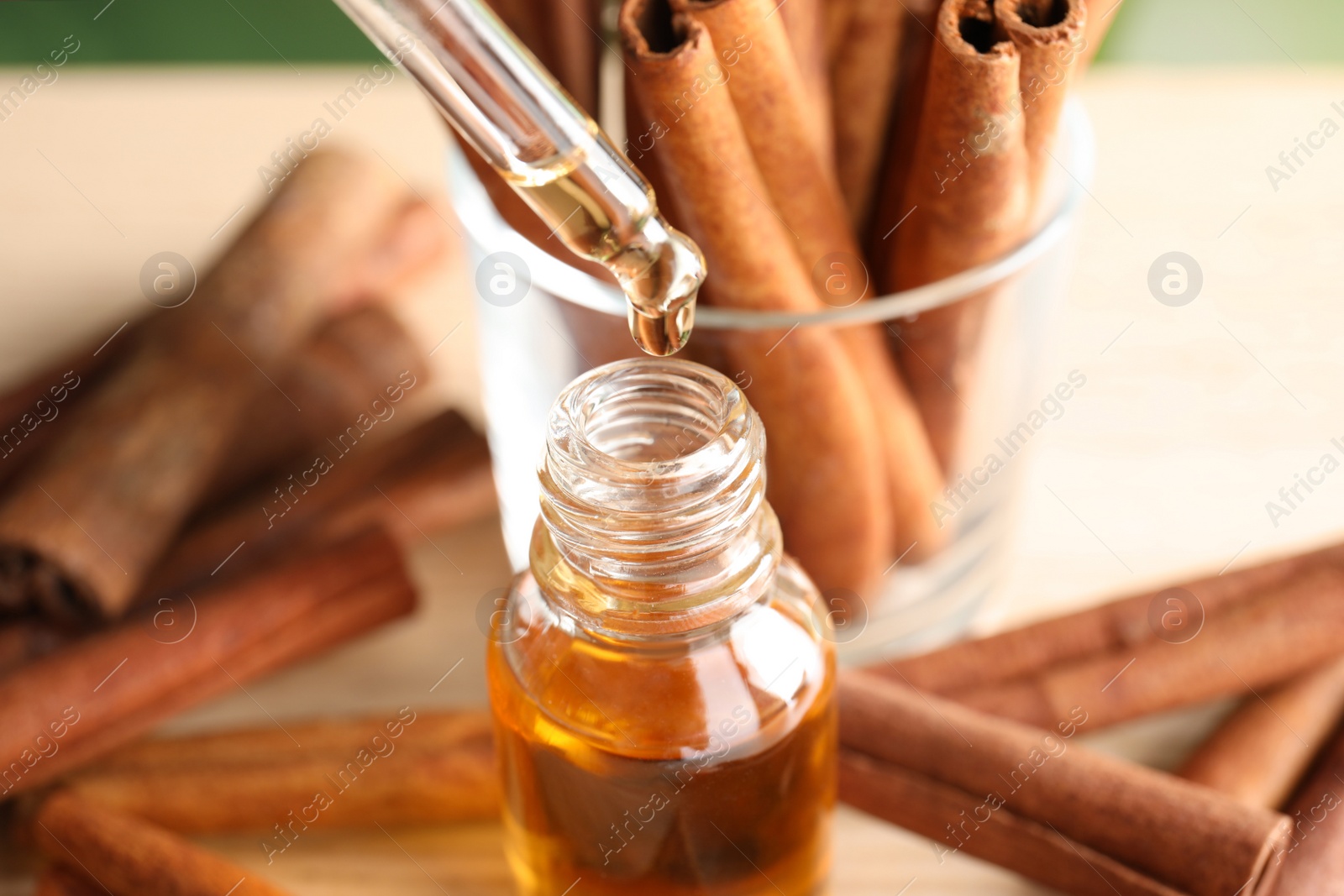 Photo of Pipette with essential oil over bottle and cinnamon sticks on table, closeup