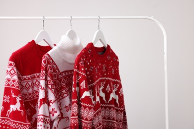 Rack with different Christmas sweaters on light background, space for text