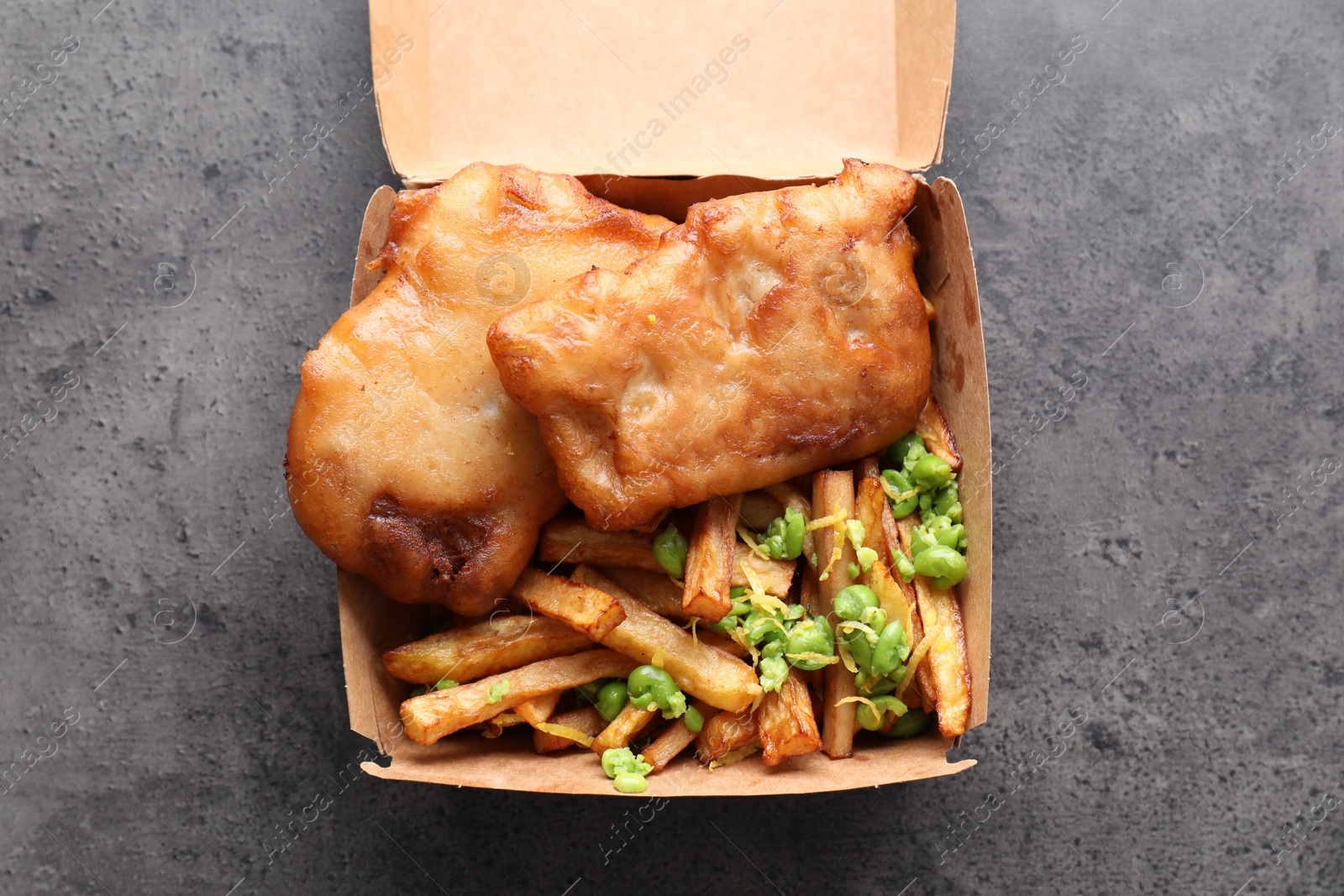 Photo of Tasty fish, chips and peas in paper box on grey table, top view