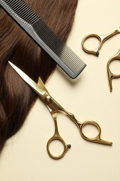 Photo of Professional scissors and comb with brown hair strand on beige background, flat lay