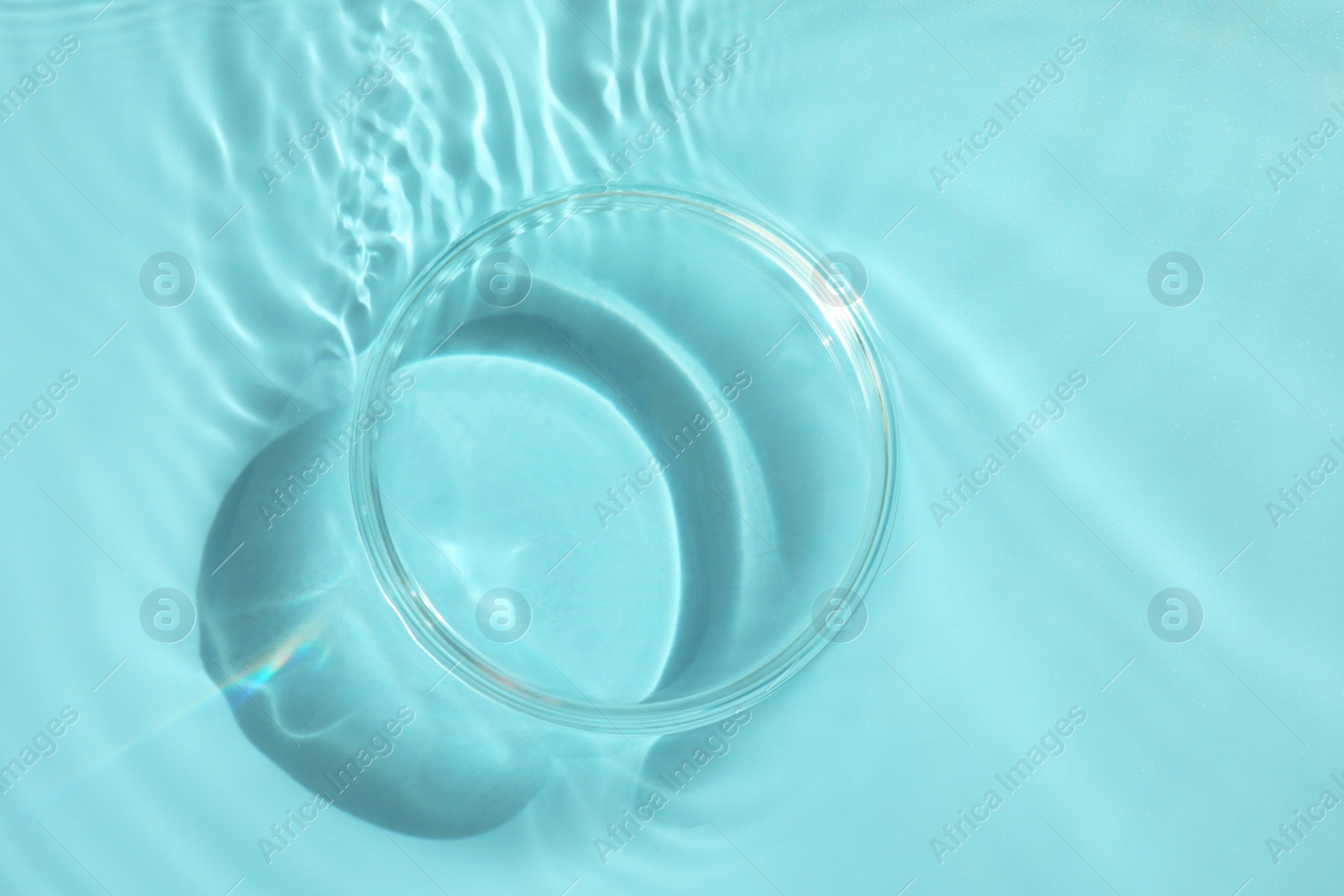 Photo of Stylish presentation for product. Glass podium in water on light blue background, top view