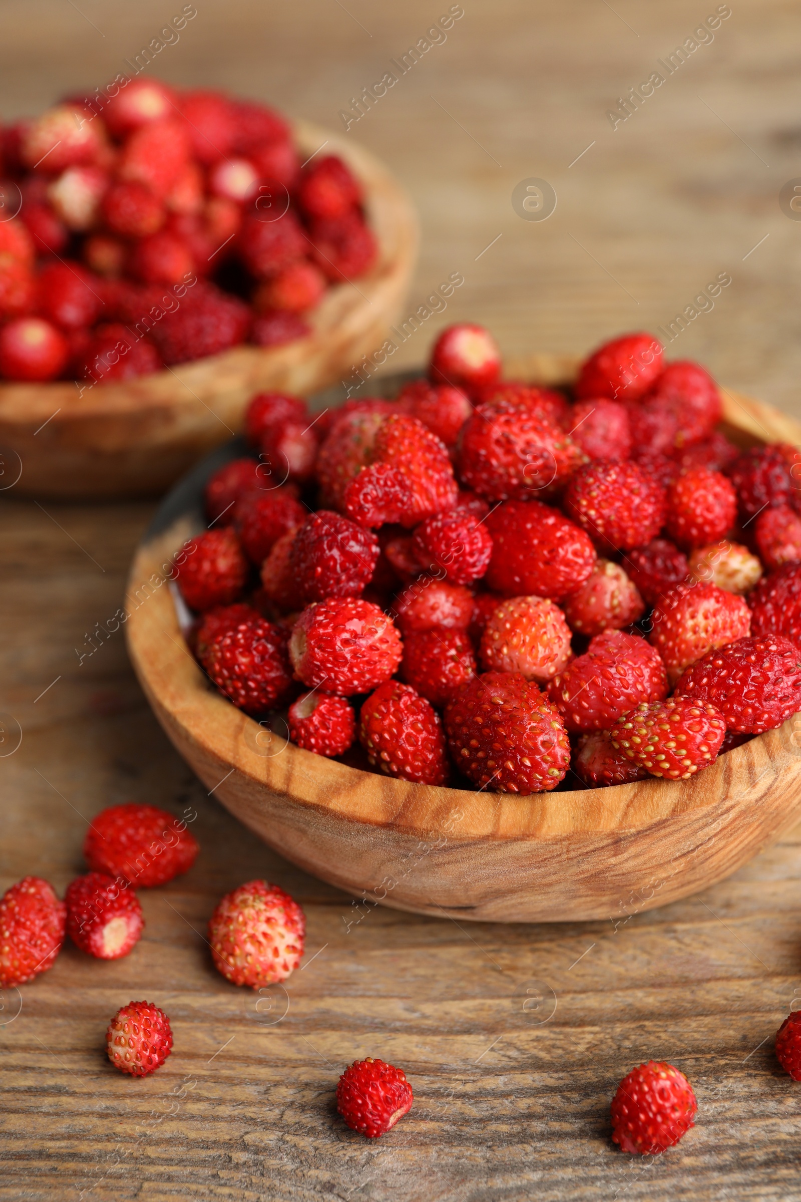 Photo of Fresh wild strawberries in bowls on wooden table