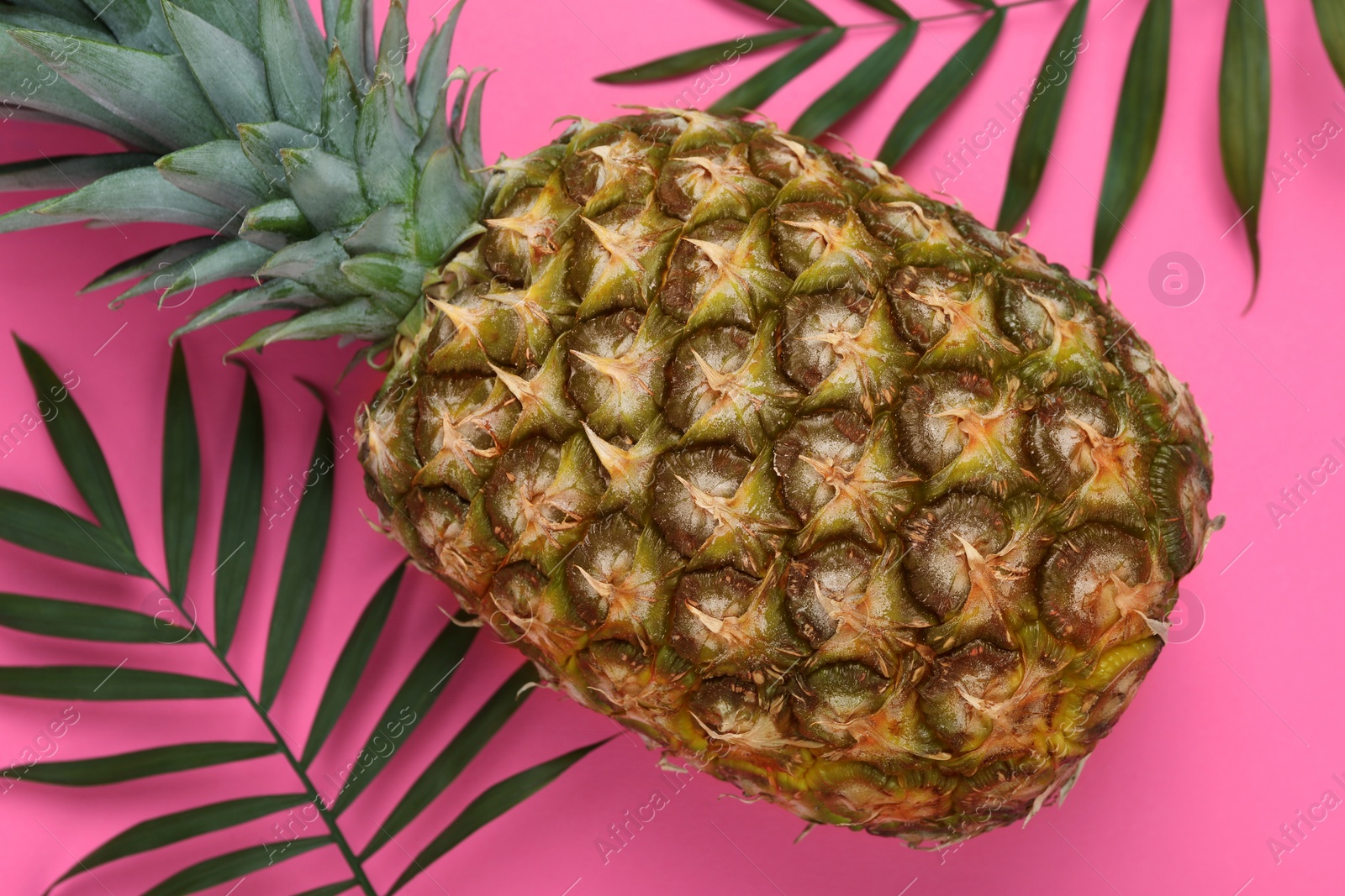Photo of Whole ripe pineapple and green leaves on pink background, flat lay