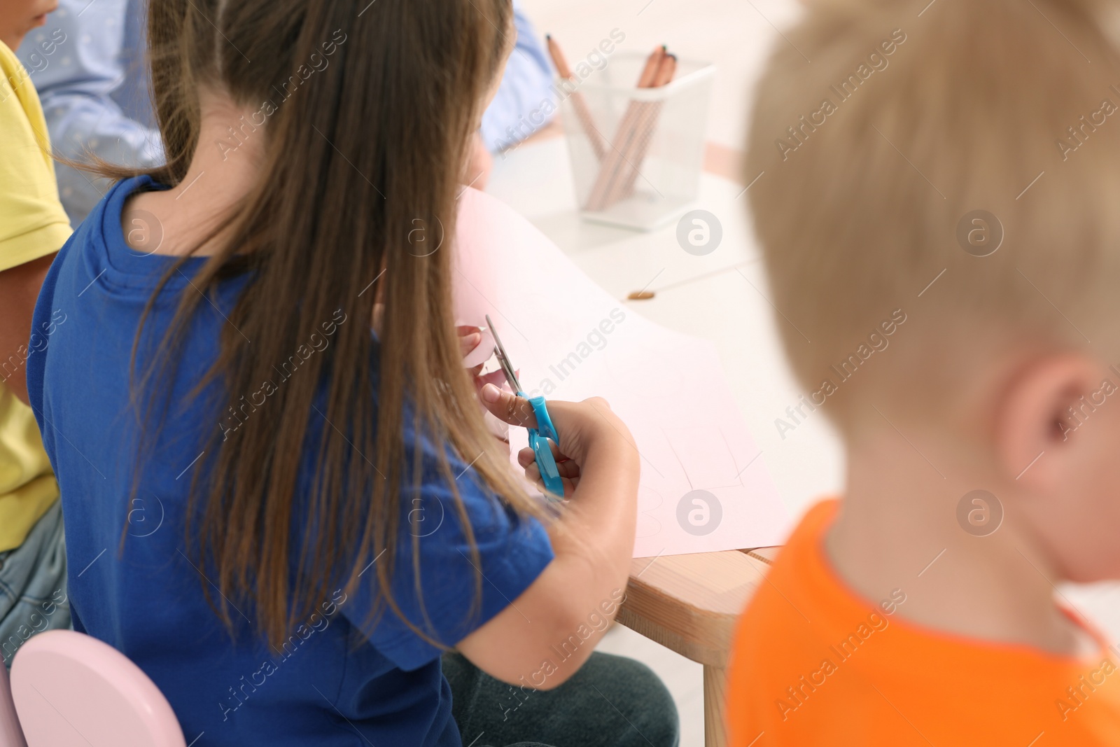 Photo of Little girl and boy cutting color paper with scissors at desk, closeup. Kindergarten activities