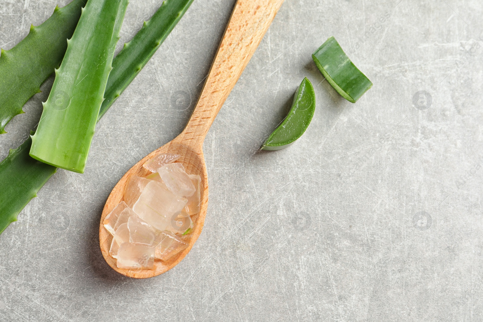 Photo of Flat lay composition with spoon of peeled aloe vera, green leaves and space for text on gray background