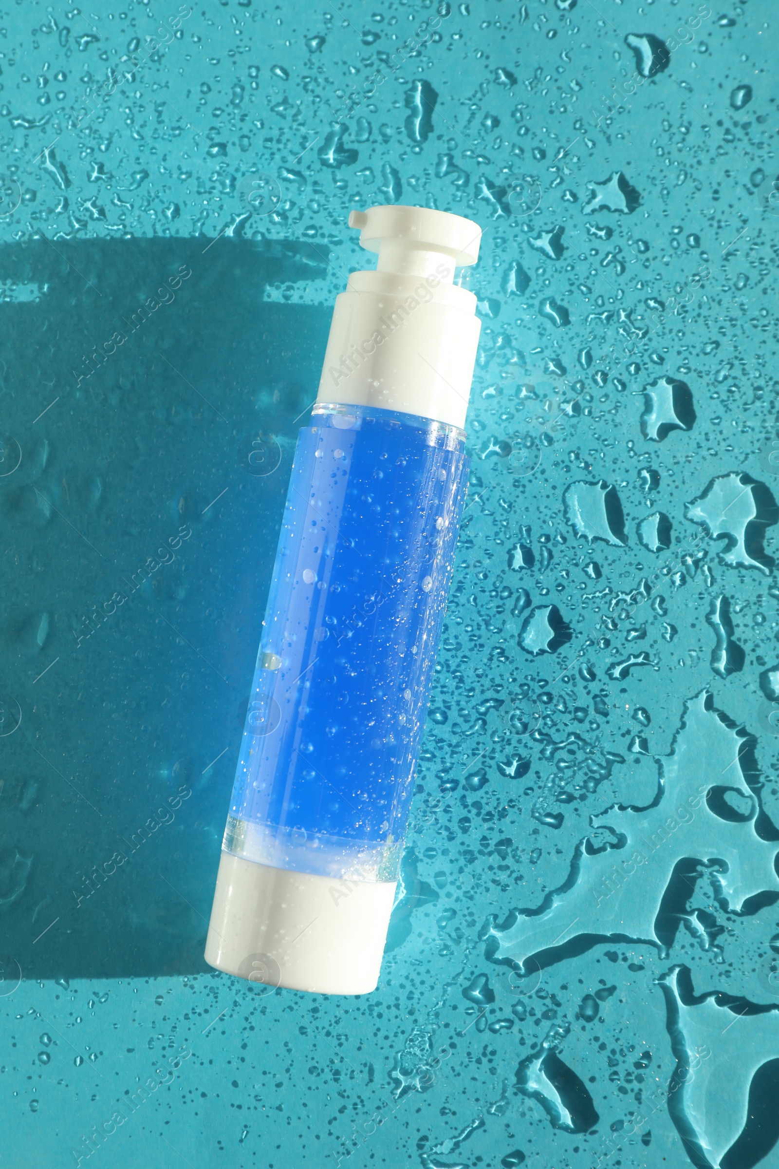 Photo of Bottle of cosmetic product on wet turquoise background, top view