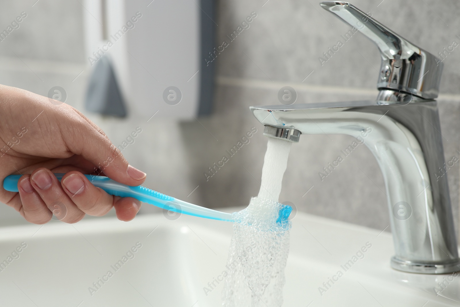 Photo of Woman washing plastic toothbrush under flowing water from faucet in bathroom, closeup