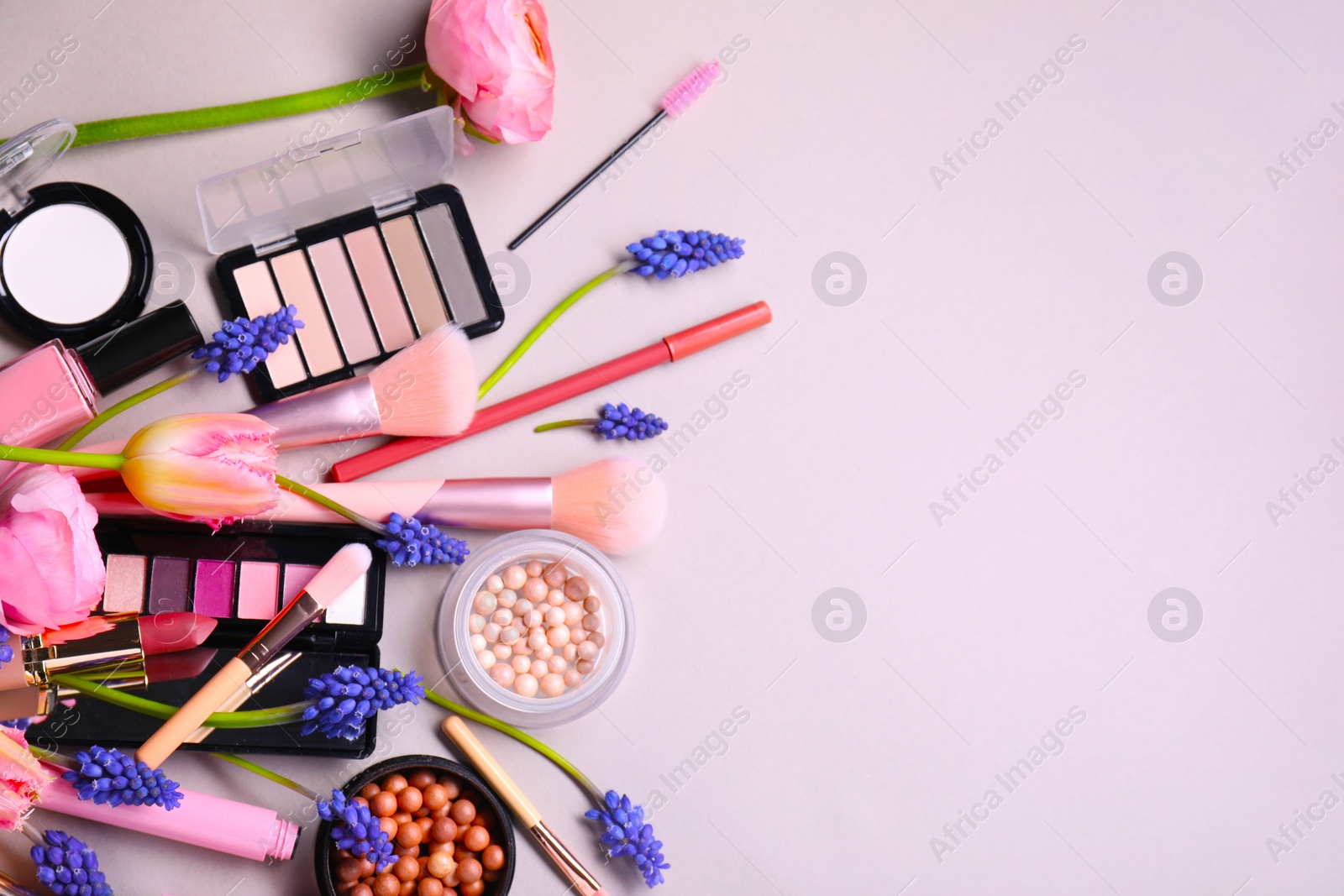 Photo of Flat lay composition with different makeup products and beautiful spring flowers on gray background, space for text