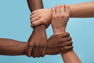 Men joining hands together on light blue background, closeup