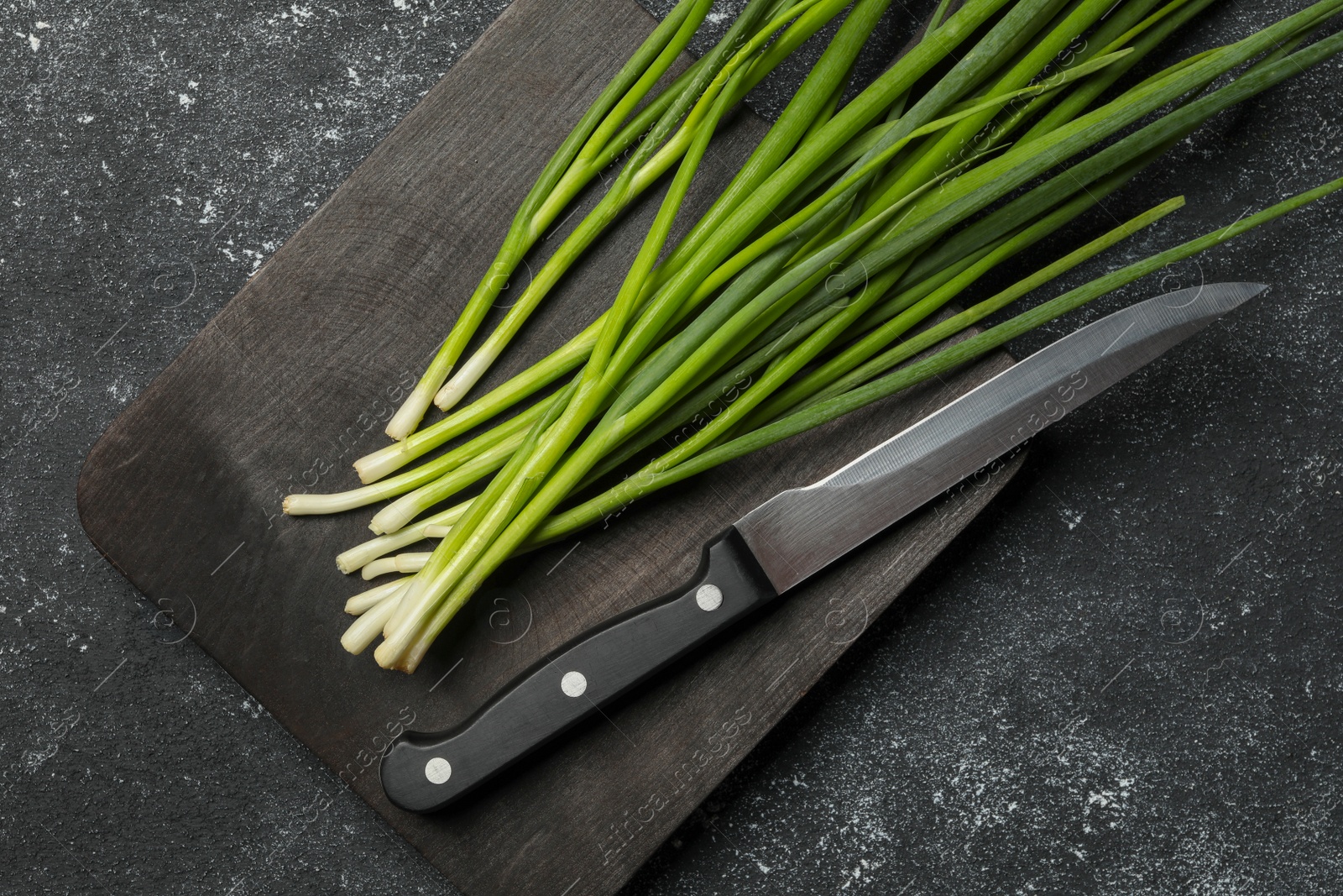 Photo of Fresh green onion and knife on black table, top view