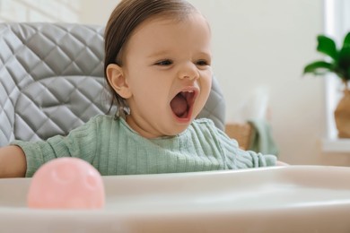 Cute little baby sitting in high chair indoors