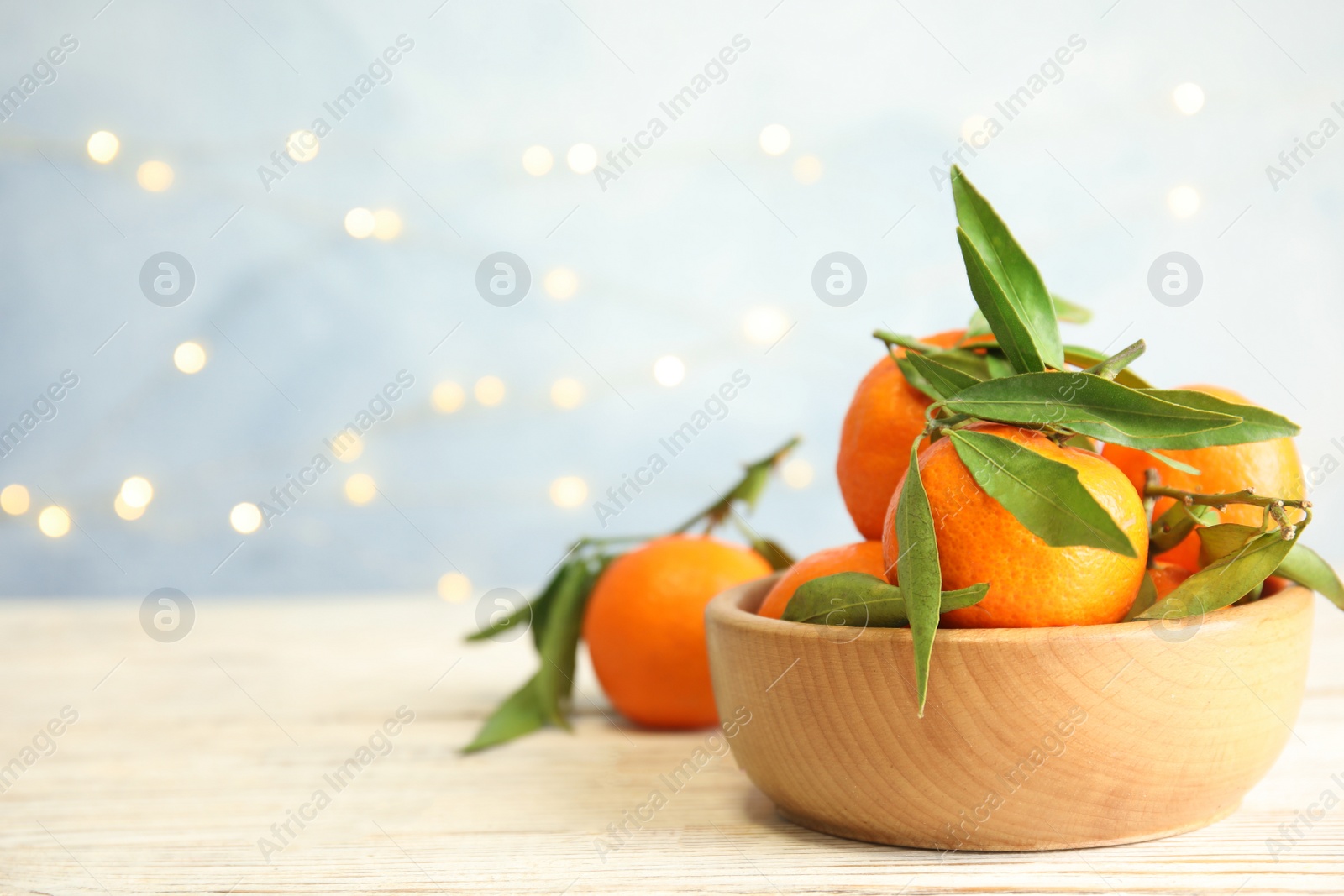 Photo of Bowl with ripe tangerines and blurred Christmas lights on background. Space for text