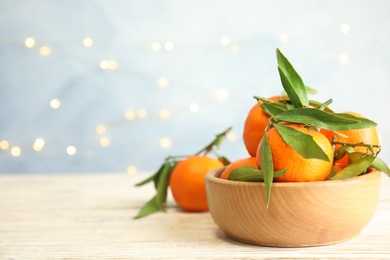 Photo of Bowl with ripe tangerines and blurred Christmas lights on background. Space for text