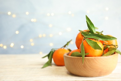 Bowl with ripe tangerines and blurred Christmas lights on background. Space for text