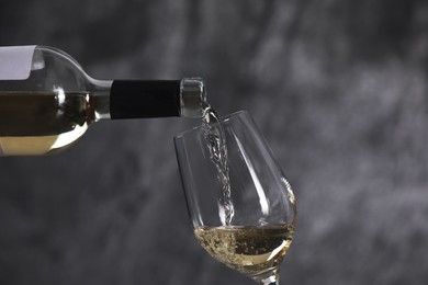 Pouring white wine from bottle into glass on grey background, closeup