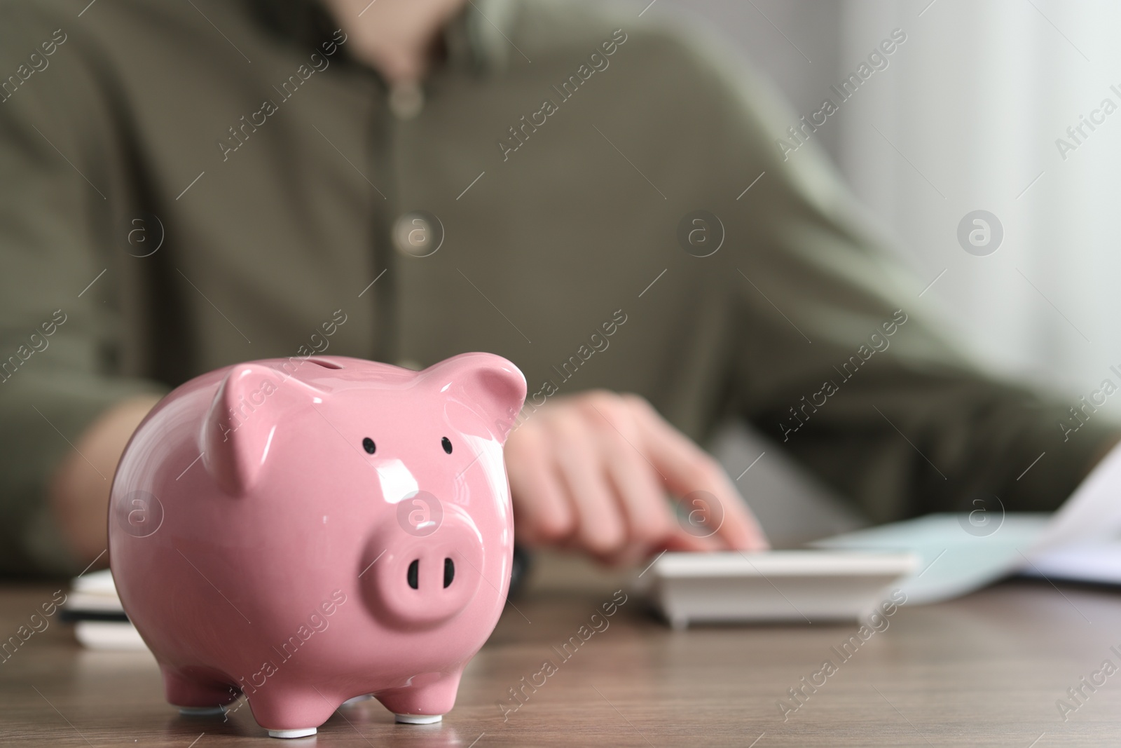 Photo of Financial savings. Man using calculator at wooden table, focus on piggy bank