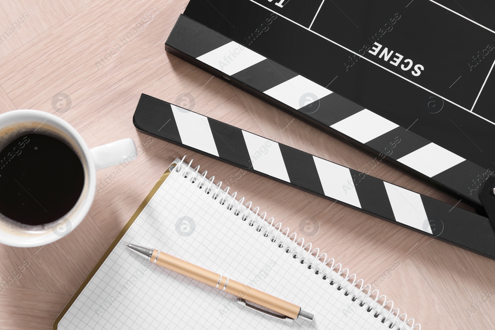 Photo of Movie clapper, coffee, notebook and pen on wooden table, flat lay