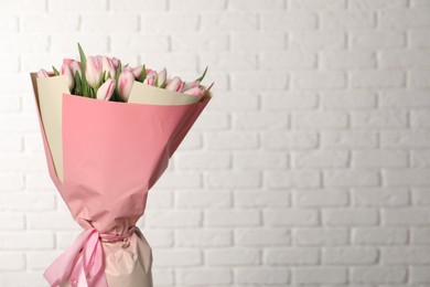 Beautiful bouquet of fresh pink tulips against white brick wall. Space for text