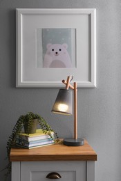 Books, lamp and beautiful plant on chest of drawers near grey wall in child room. Interior design