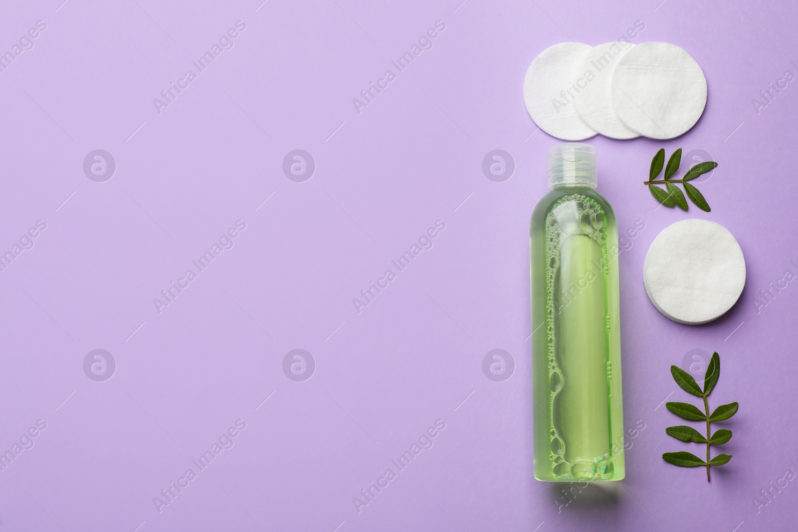 Photo of Cotton pads, leaves and makeup removal product on violet background, flat lay. Space for text