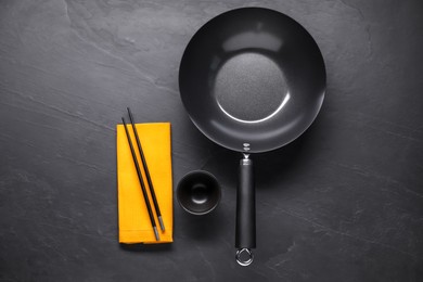 Empty iron wok, sauce bowl and chopsticks on black table, flat lay