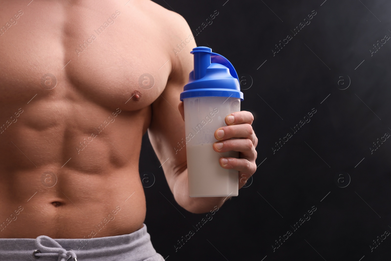 Photo of Young man with muscular body holding shaker of protein on dark grey background, closeup. Space for text