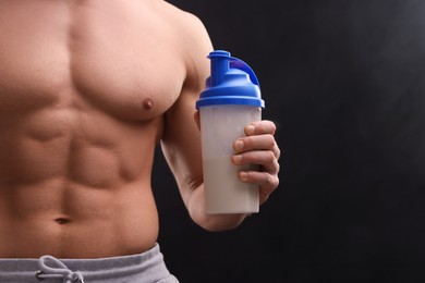 Photo of Young man with muscular body holding shaker of protein on dark grey background, closeup. Space for text