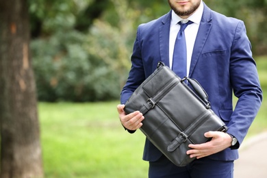 Photo of Businessman with black briefcase in hands outdoors. Space for text